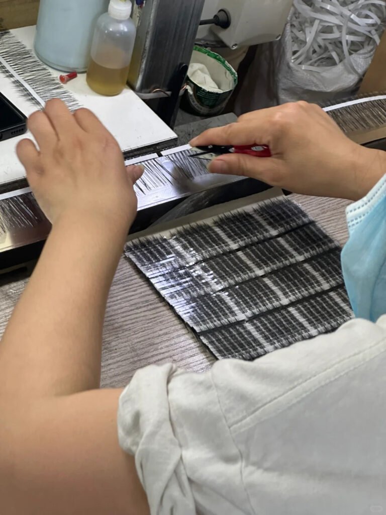 A skilled technician performs precise, hand-finishing quality control on strip lashes at the Shewincosmetic manufacturing facility in Qingdao Pingdu, the global hub for false eyelash production.
