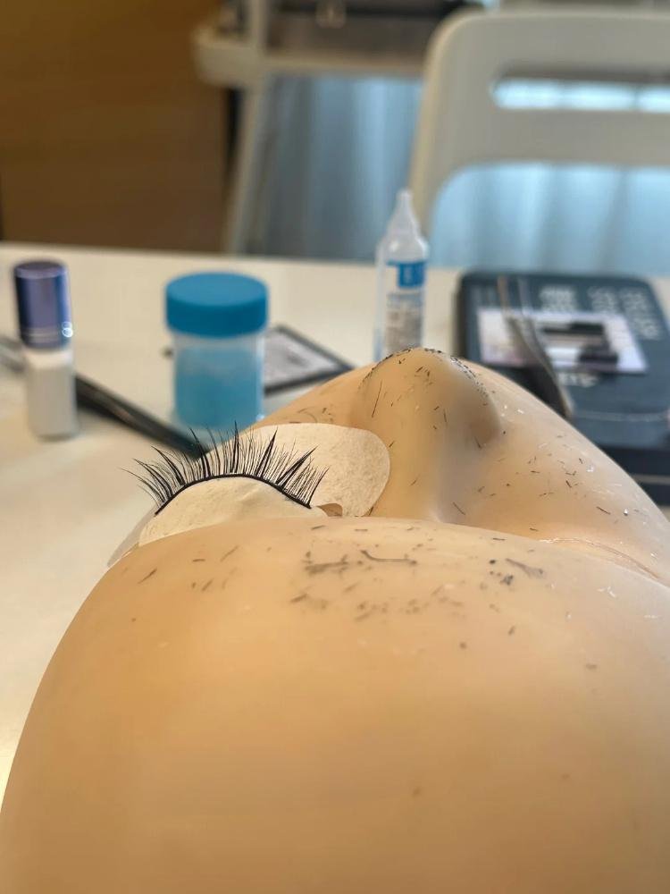 A student applying eyelash extensions on a practice mannequin head during an Eyelash Extension Training Course